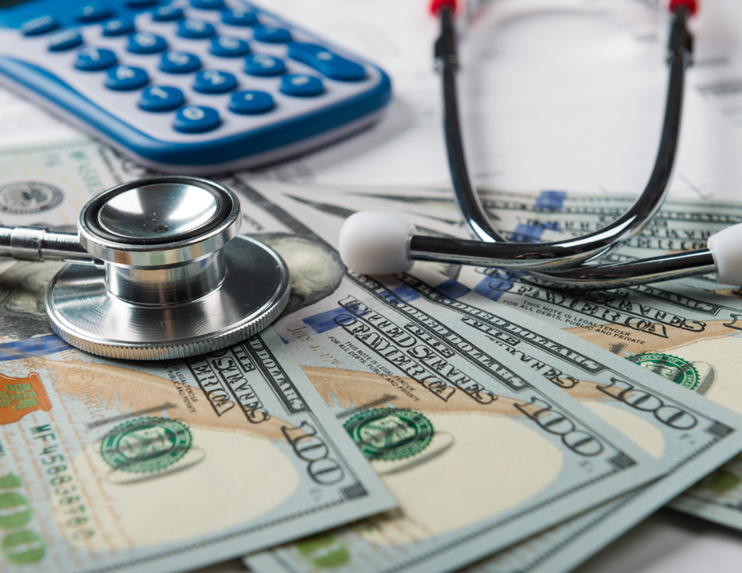 Dollar bills with a calculator and stethoscope laying on it.