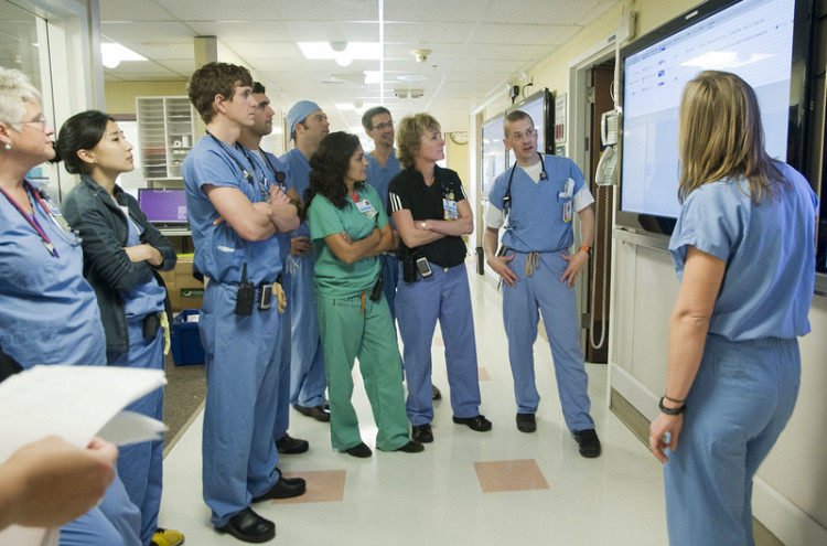 A group of medical students gather around a tv screen while a physician presents information.